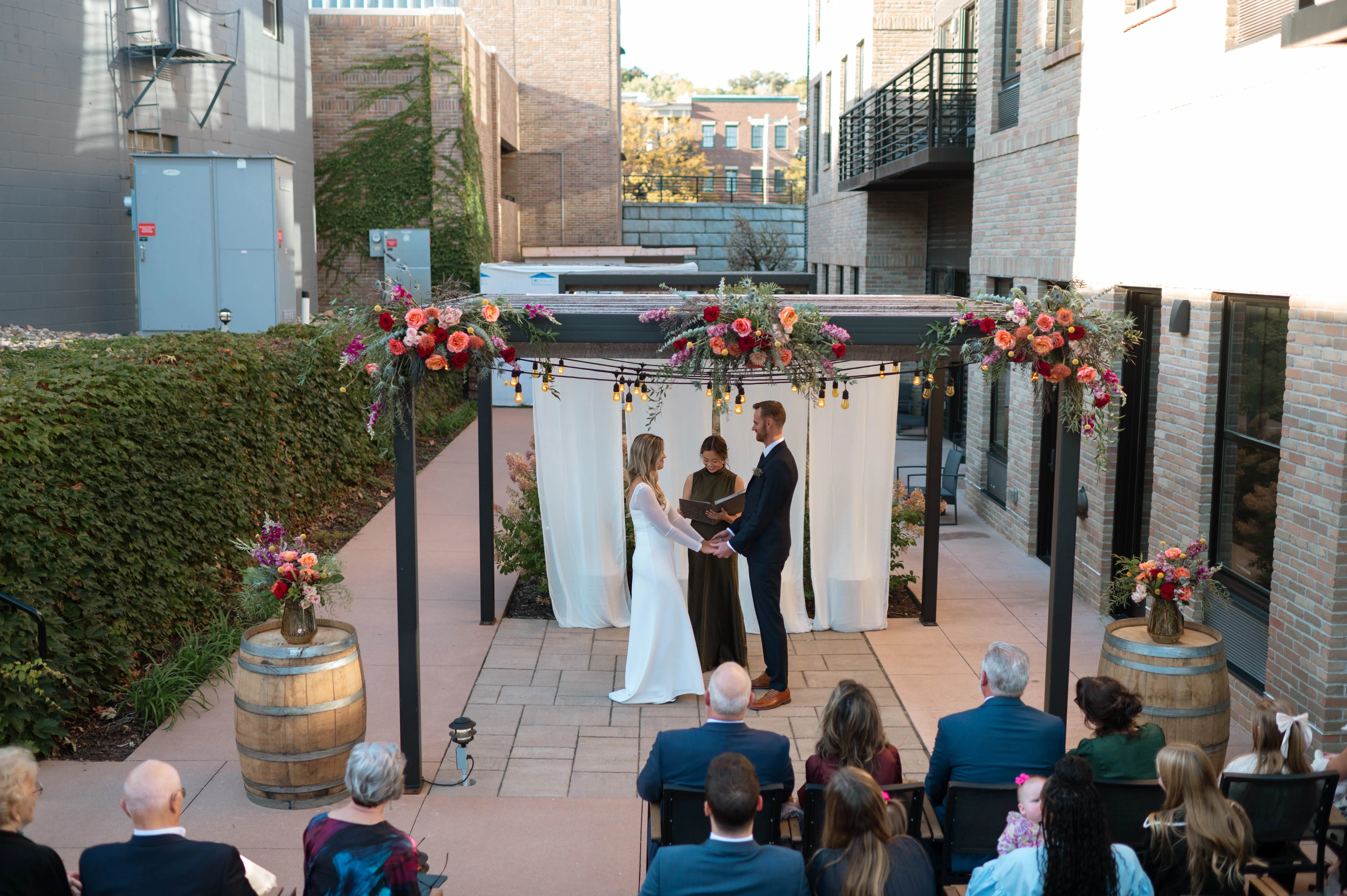 Wide view of the ceremony beneath Hotel Crosby's pergola, jewel-toned florals framing the vows