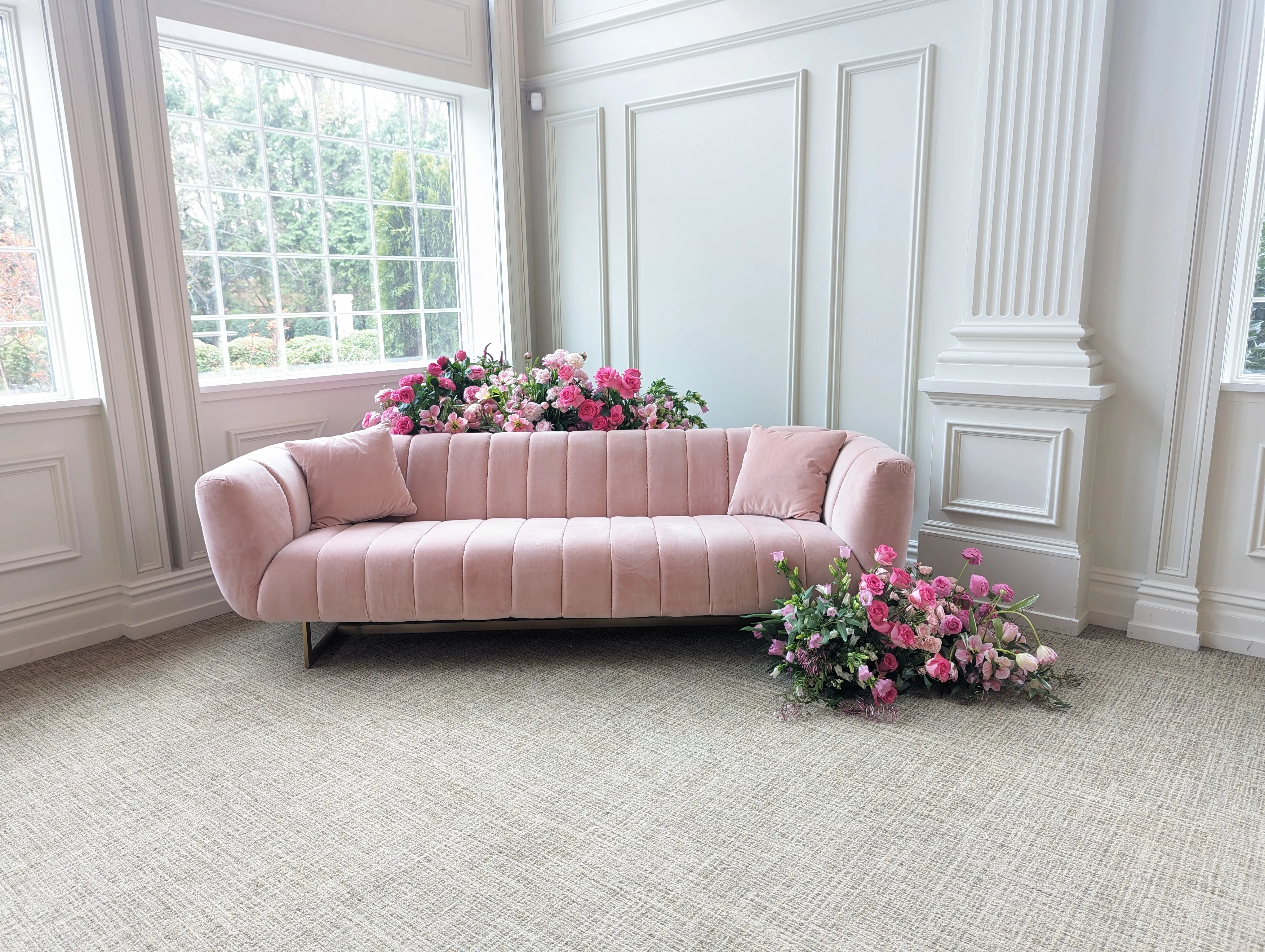 A blush velvet sofa in the lounge, dressed with a garland of pink florals along its back