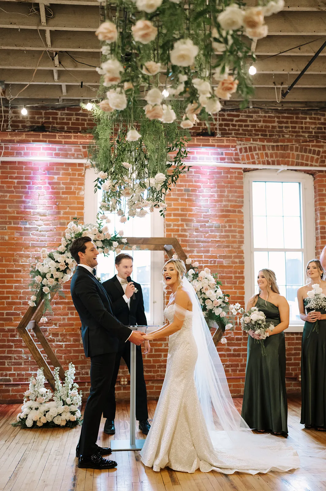 Claire and Connor exchange vows beneath a hexagon arbor dressed in ivory and blush roses at The JX Event Venue