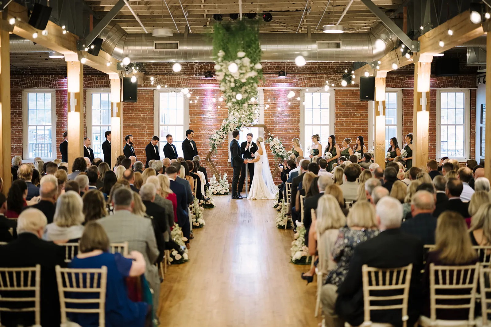 Wide view of a wedding ceremony aisle with a hexagon arbor floral installation at The JX Event Venue, Stillwater