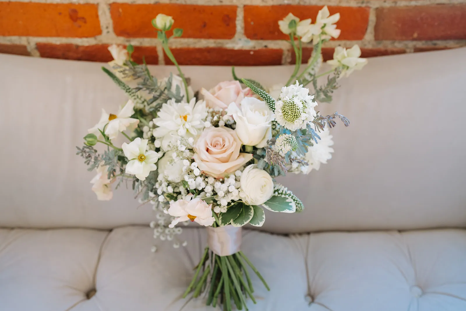 Bridal bouquet resting on a vintage sofa against exposed brick at The JX Event Venue, Stillwater