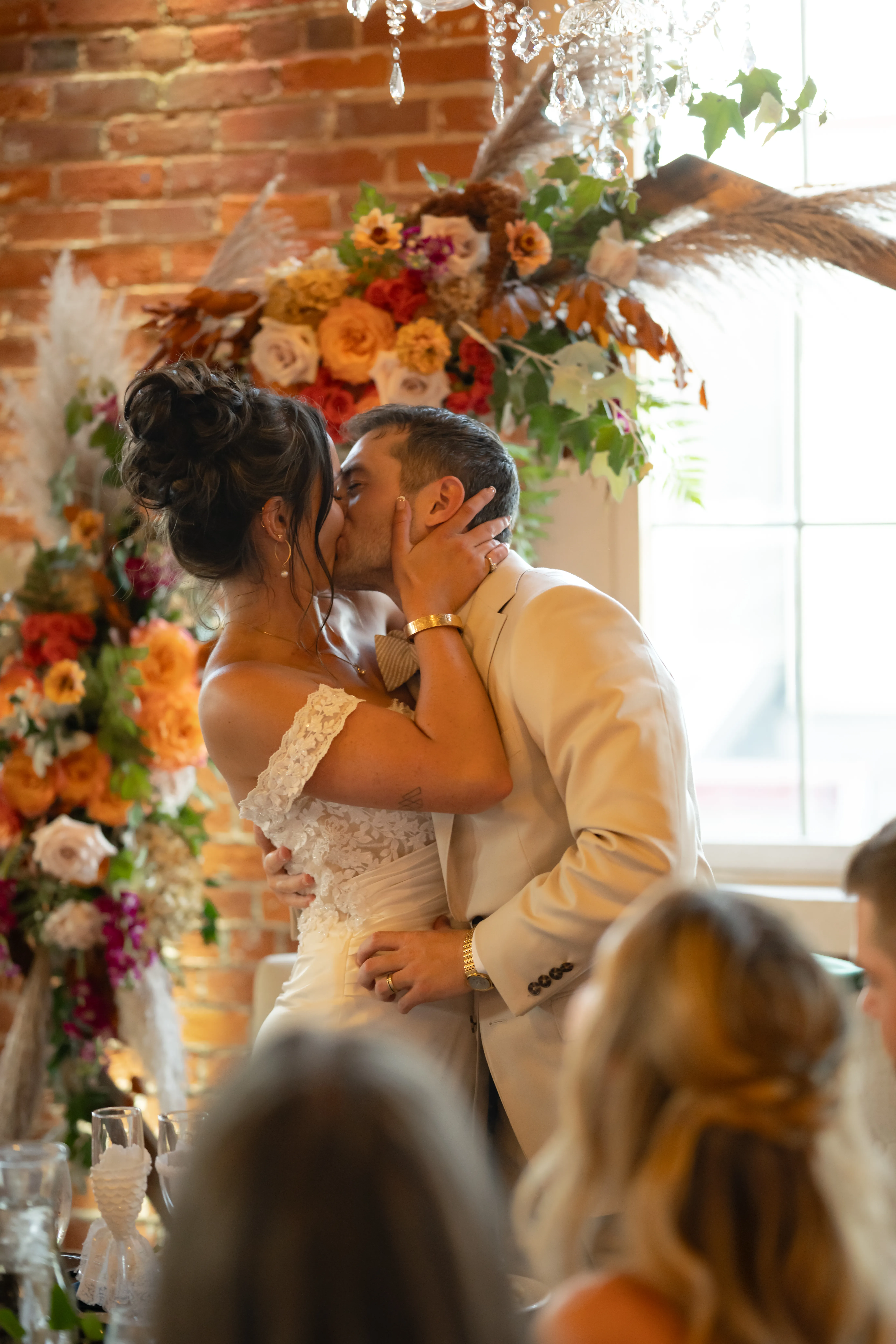 Katie and Kurt kiss beneath the repurposed ceremony arch, indoors at The JX