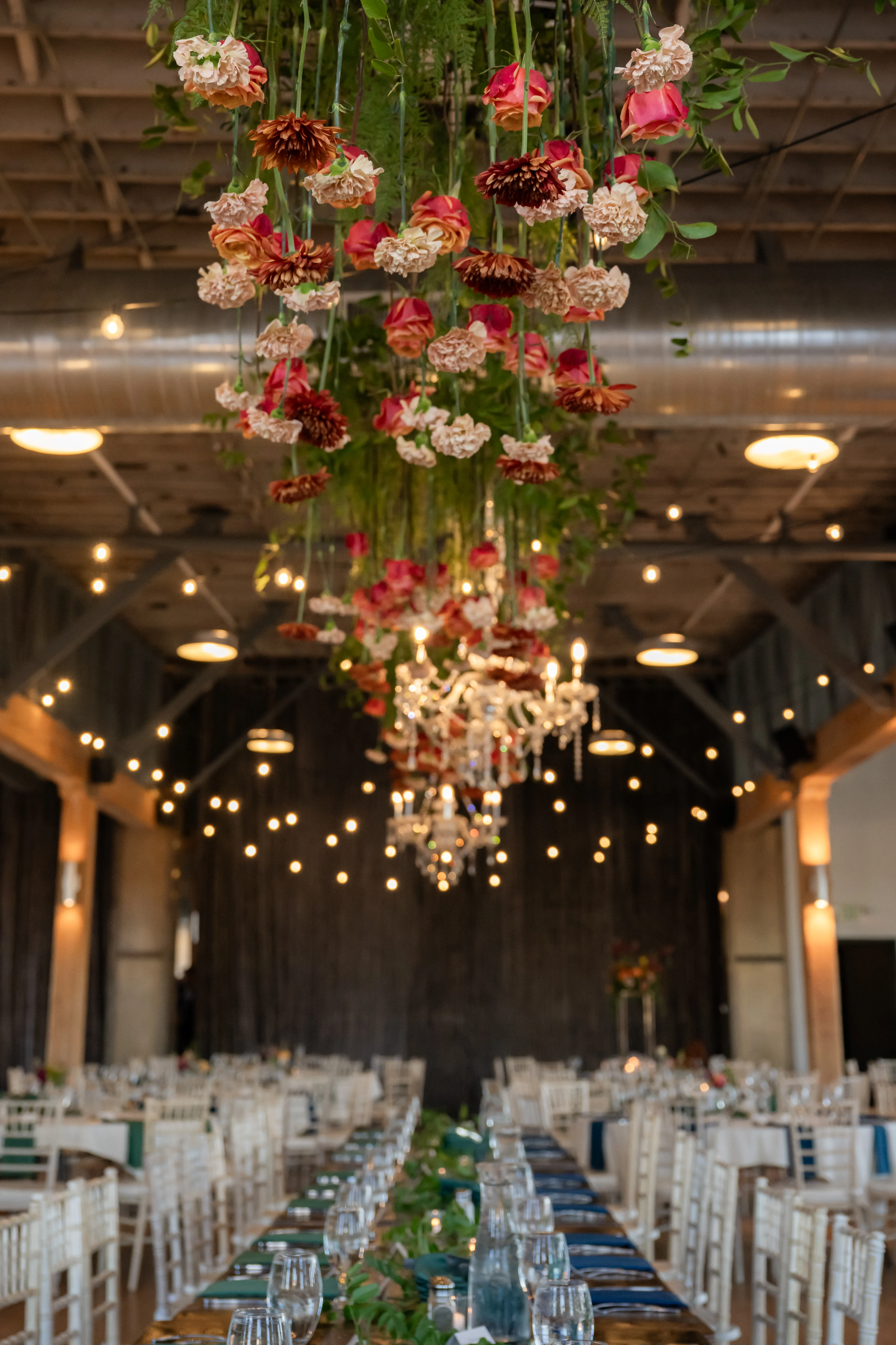 Wide view of the reception's hanging floral chandelier above the head table at The JX
