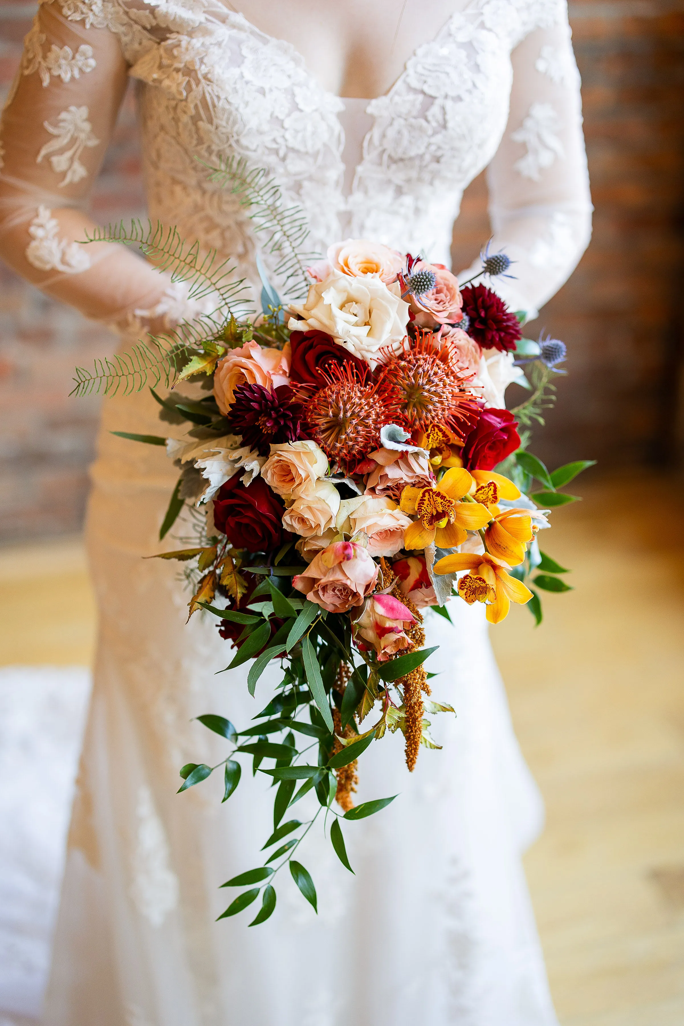 Close-up of Angela's cascading bouquet of burgundy dahlias, garden roses, and pincushion protea against her lace gown