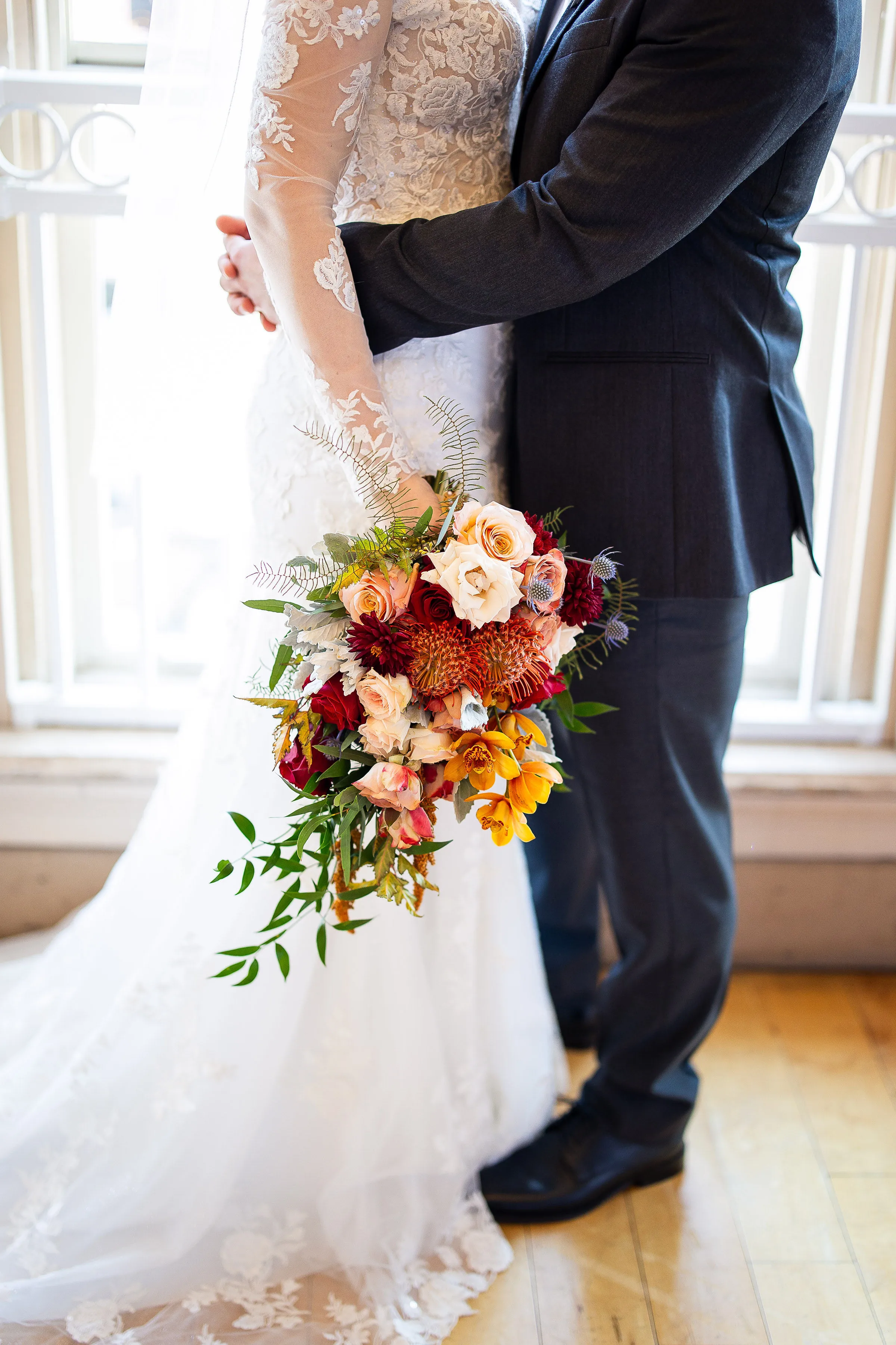 Angela and Nick share an embrace in warm window light, her cascading bouquet between them