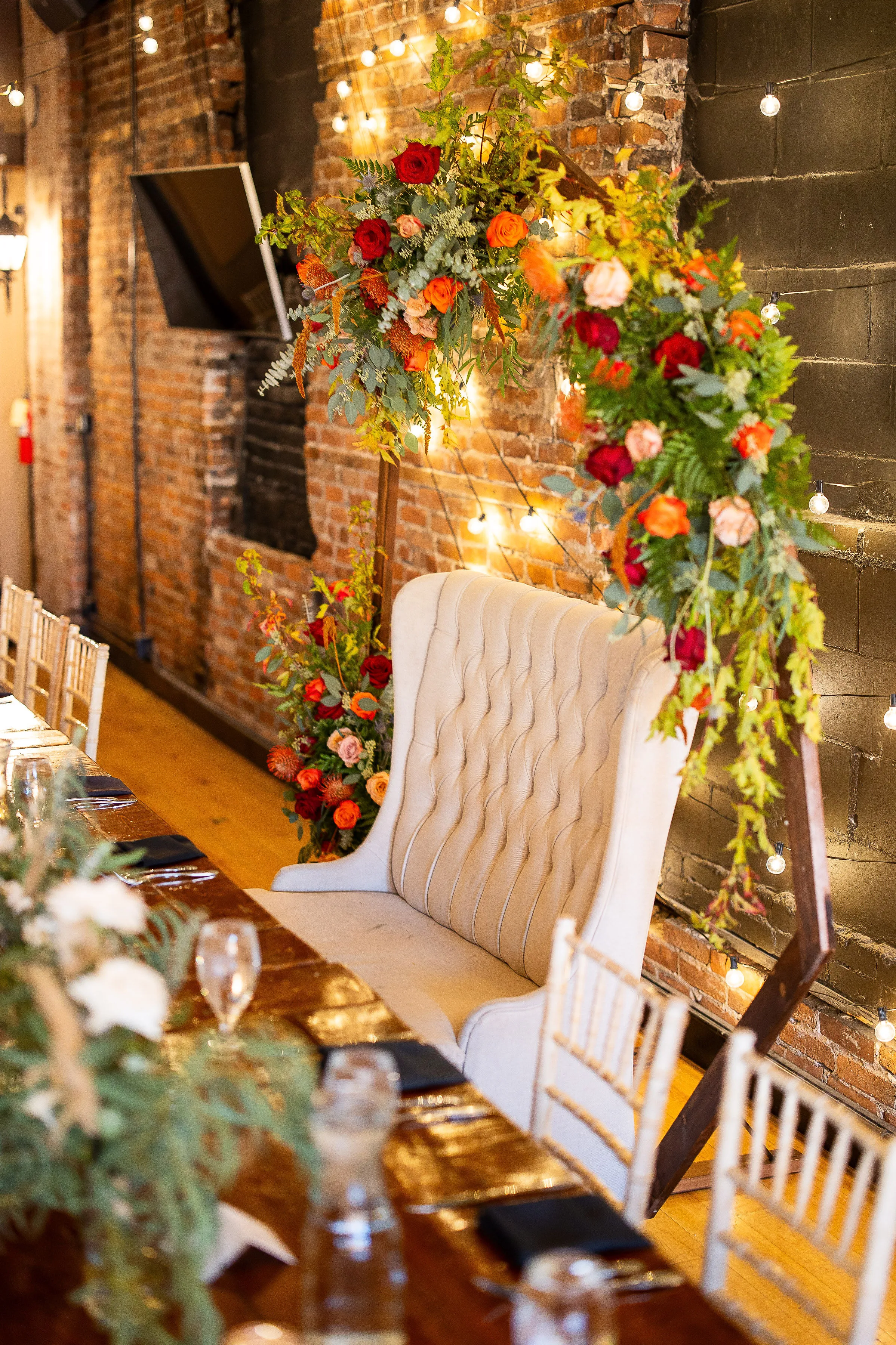 The ceremony arch repurposed behind the sweetheart bench at the reception, framed by Loft 214's exposed brick and string lights