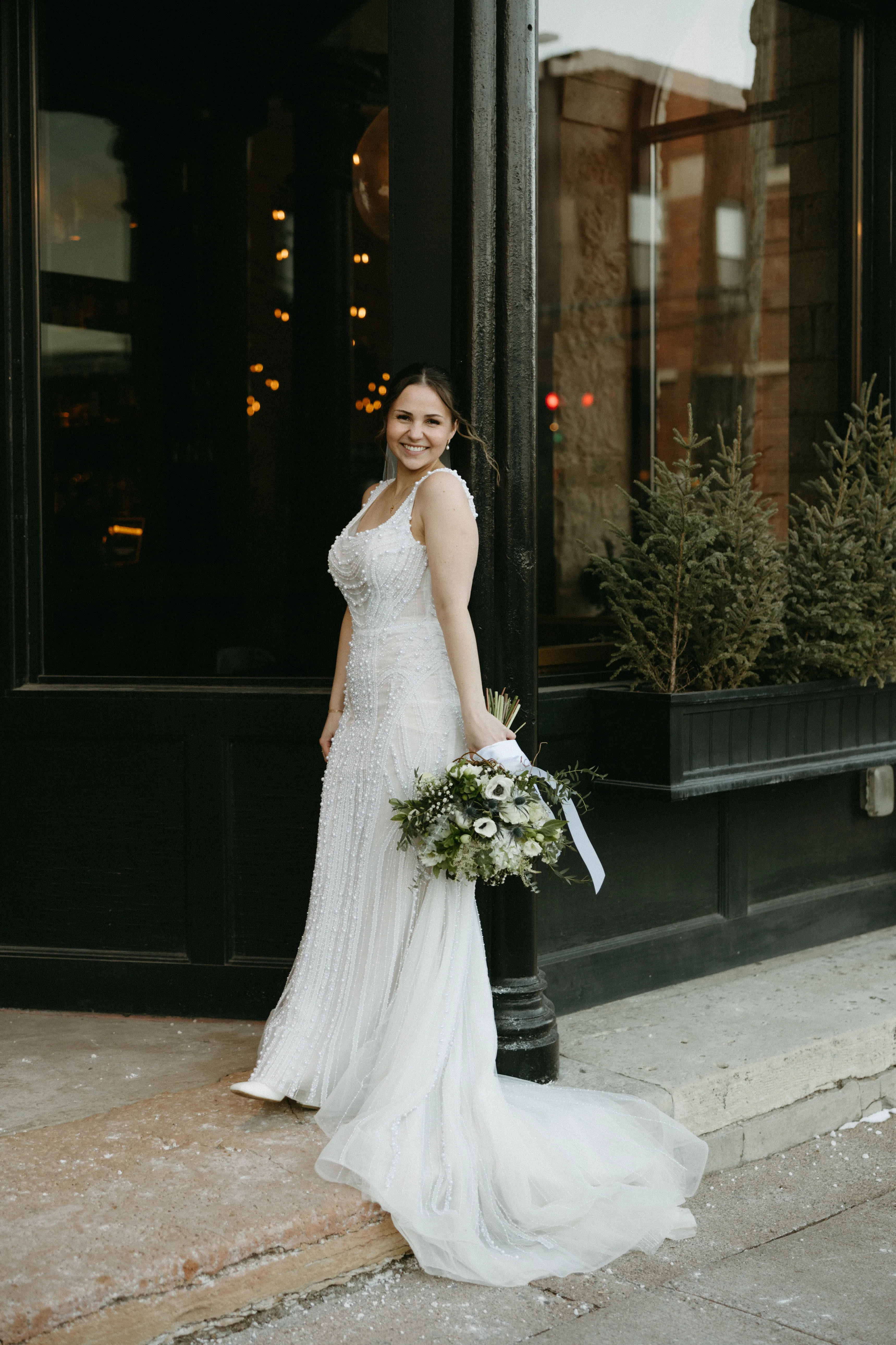 Allie in her beaded gown and fur coat, bouquet in hand, outside a downtown Stillwater storefront