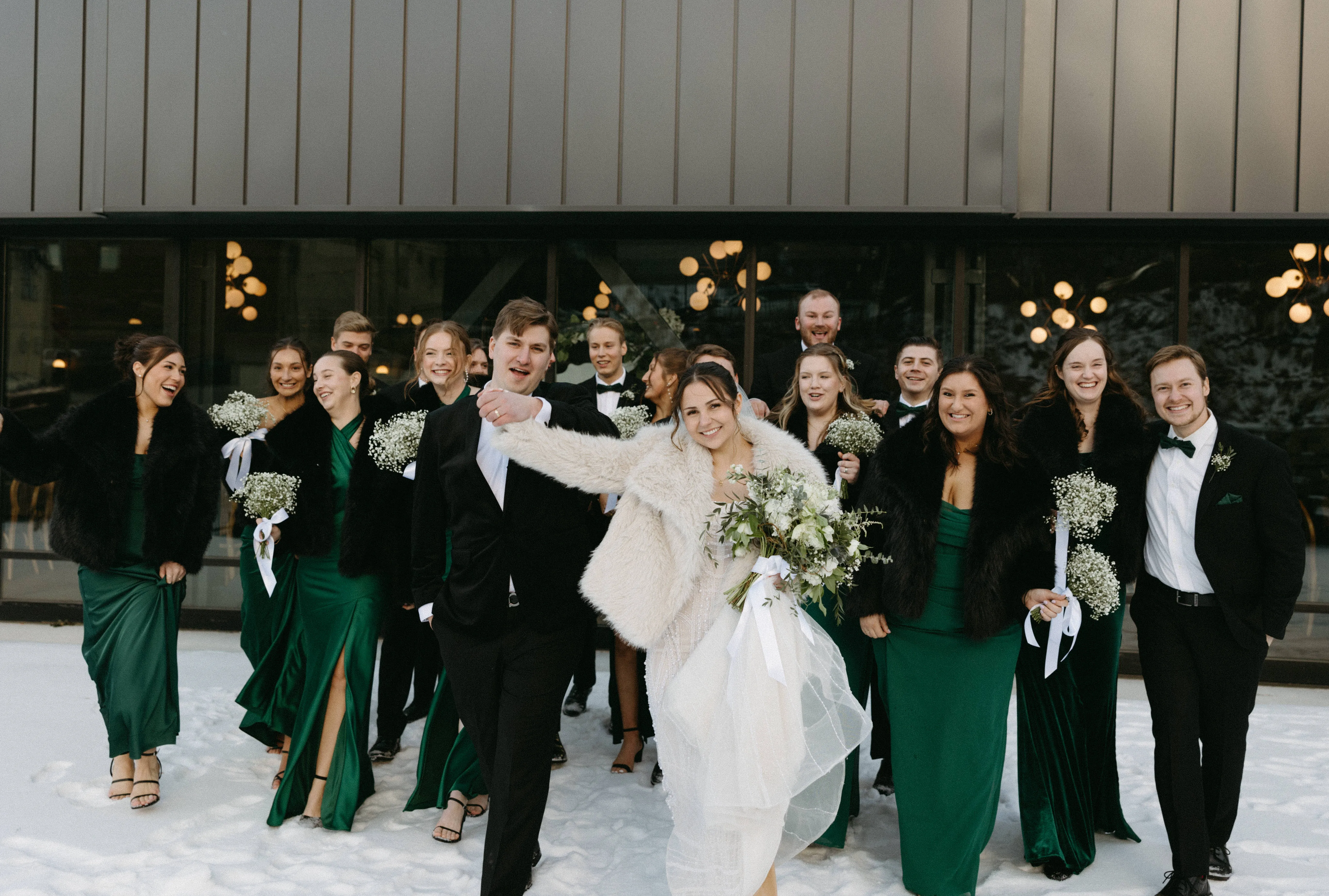 The wedding party walking and cheering through the snow outside The Lora