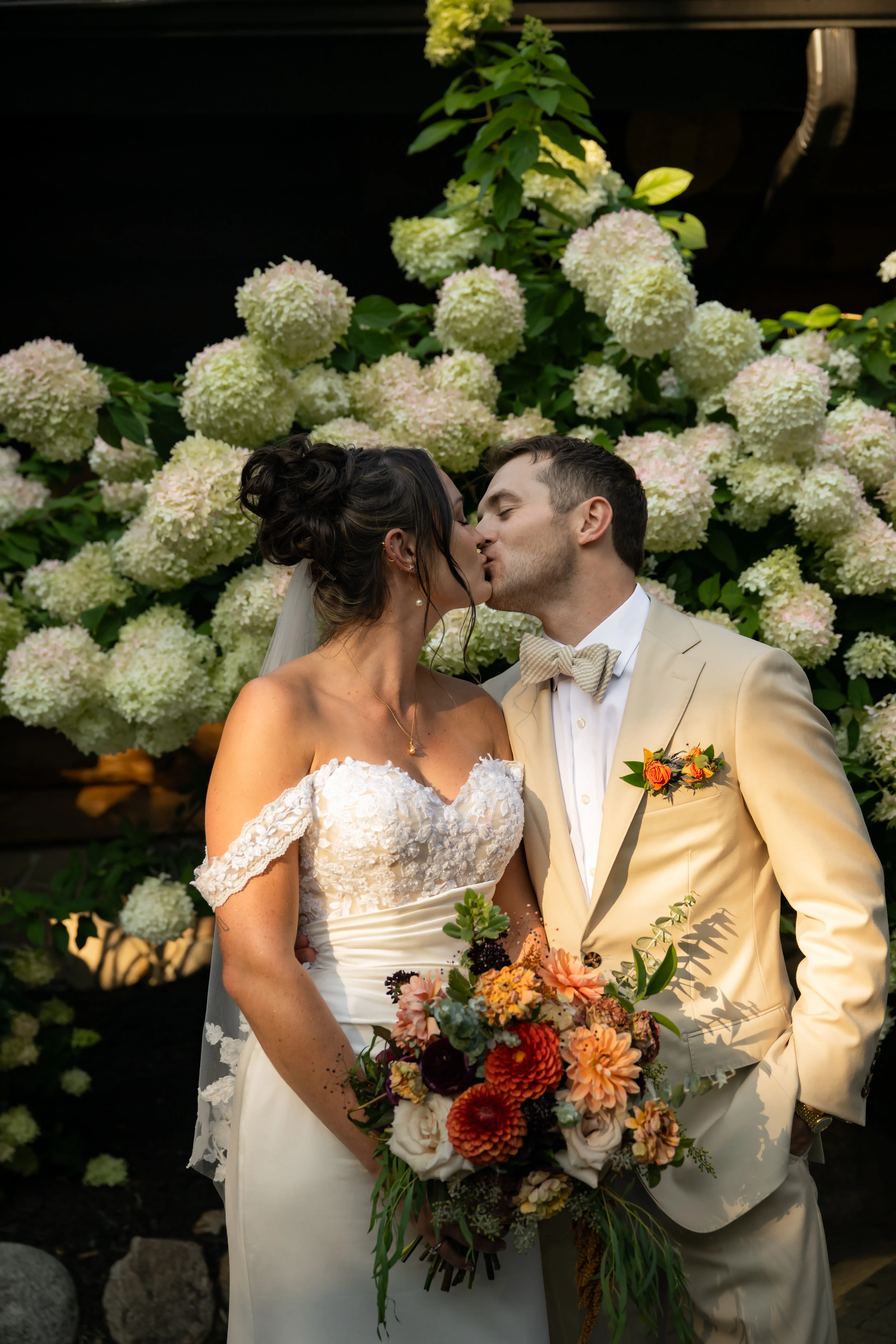 A kiss beside a hydrangea hedge, Katie's bouquet held between them